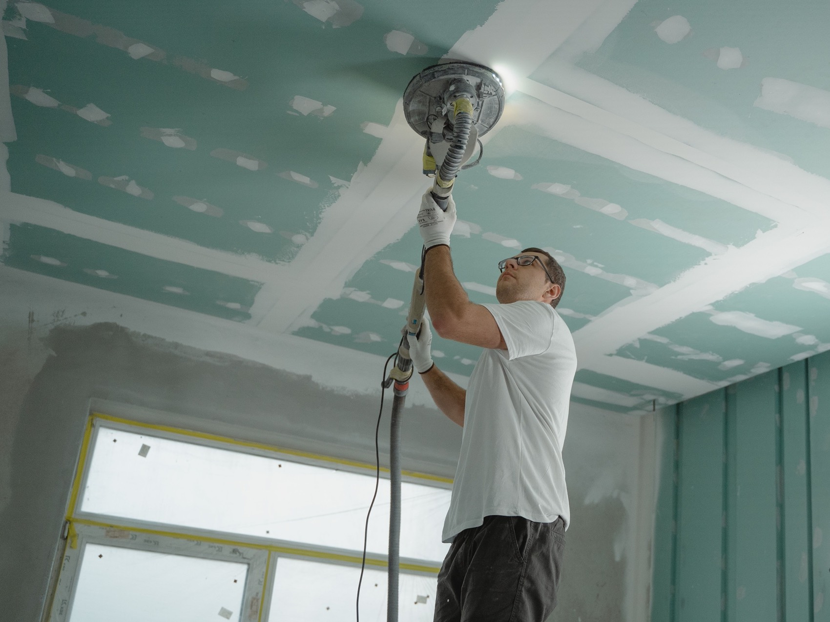 Plaquiste de Neo Construction 24 ponçant les bandes de placo avant peinture