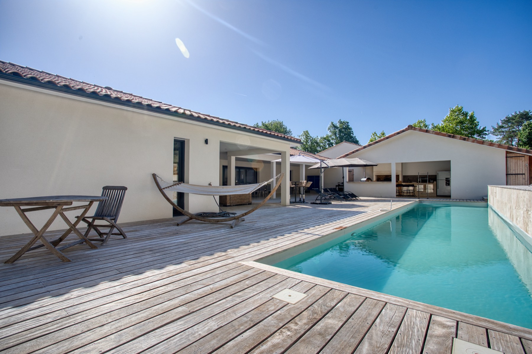 Terrasse bois, piscine et cuisine d'été d'une villa réalisée par Neo Construction 24